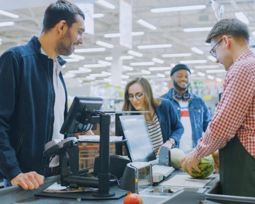 man-checkered-shirt-stands-cashier-while-customer-checks-his-produce